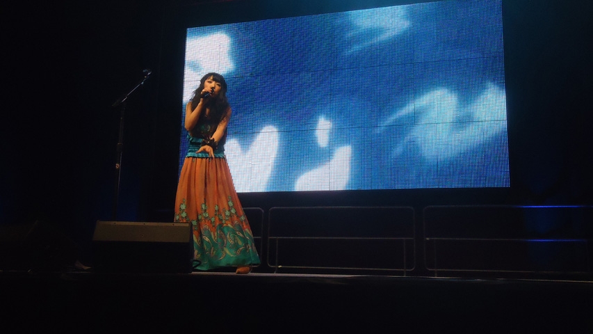 Ito sings in front of a giant Nitro+-themed screen.